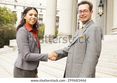 Business people or lawyers on outdoor steps shaking hands. Focus is on faces.