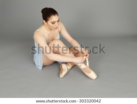 A seated ballerina tying up her ballet slipper.