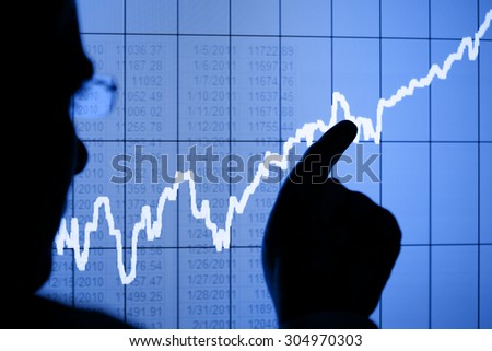 Silhouette of a man pointing to a rising graph on an LCD display. Focus is on the LCD display. Chart created by the photographer.