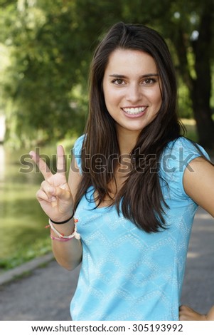 An attractive young woman smiles and gives the peace sign.