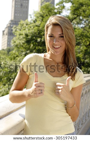 Beautiful young woman giving thumbs up on Bow Bridge in Central Park.