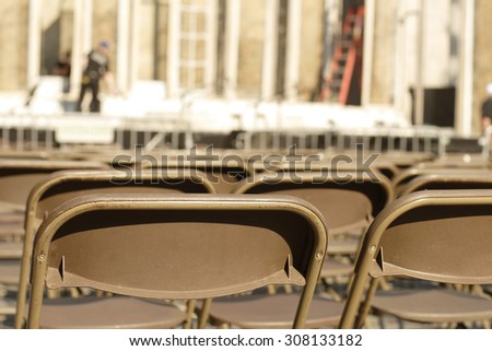 Focus on empty chairs with stage preparations in the background.