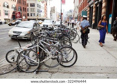 New York, New York, USA - July 14, 2011: A group of locked parked bicycles on Lafayette Street in lower Manhattan. A policeman and others can be seen on the sidewalk. There are cars in the street.
