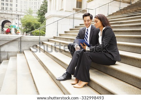 Two well dressed professionals working together outdoors. Woman shows man something on a clipboard Could be lawyers, business people etc.