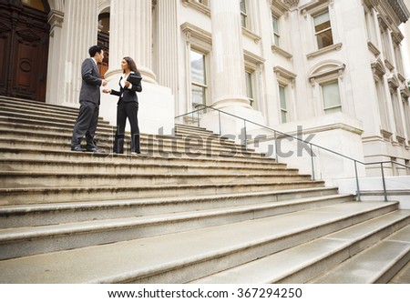 Two well dressed professionals in discussion on the exterior steps of a building. Could be lawyers, business people etc.