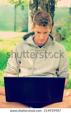 Handsome, young man working on his laptop under the tree