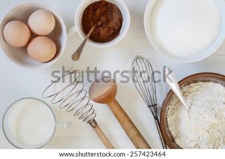 Baking ingredients on a table: eggs, flour, milk, sugar, cacao.