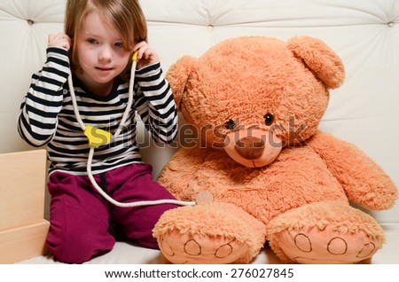 Cute, blonde girl playing doctor with plush toy bear