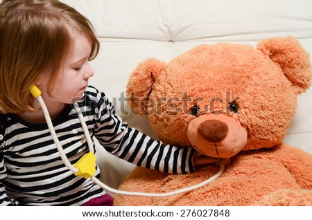 Cute, blonde girl playing doctor with plush toy bear