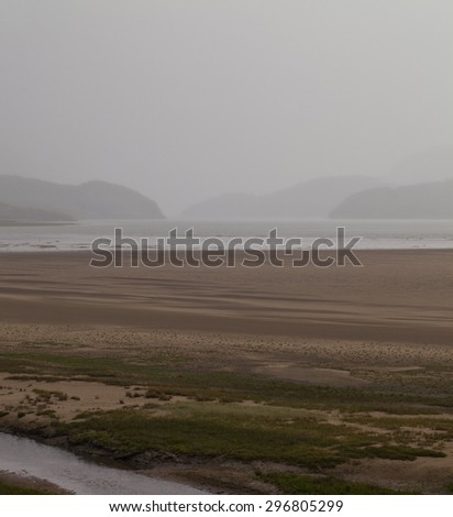 Barmouth, United Kingdom - June 28, 2015: The river Mawddach at low tide. The rain beats down on the exposed sand bars and the mountains in the distance become shadowy ghost shapes through the gloom.
