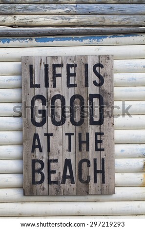 Beach Sign\
Planks of wood, nailed together and weathered then written upon hang on the side of a wooden beach hut painted in white and also weathered.The colors and weathering is iconic of the beach.