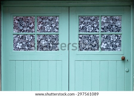Teal Door with Flowery Windows,\
A delightful double windowed door painted teal with flowery laminate on the windows.