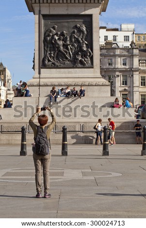 London, United Kingdom - July 10, 2015: Around the base of Lord Nelson\'s column tourist gather, sit and take photos of each other and the landmarks. Taking  with a short depth of field.