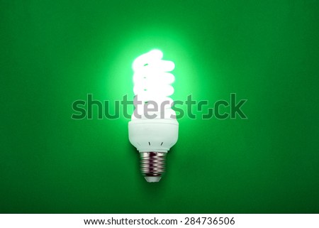 Energy saving compact fluorescent light bulb glowing on green.