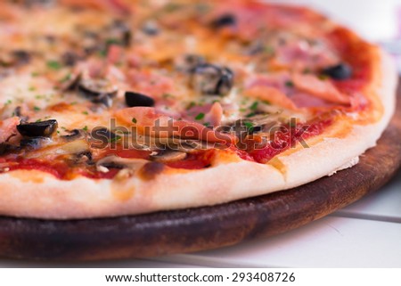 Delicious hot pizza with ham and mushrooms on wooden plate, close up. DOF