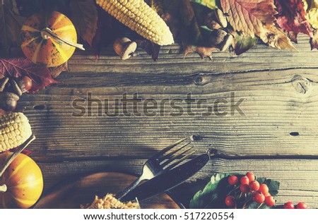Autumn background from fallen leaves and fruits with vintage place setting on old wooden table. Thanksgiving day concept, a gala dinner on the day of Thanksgiving. Free space for text.