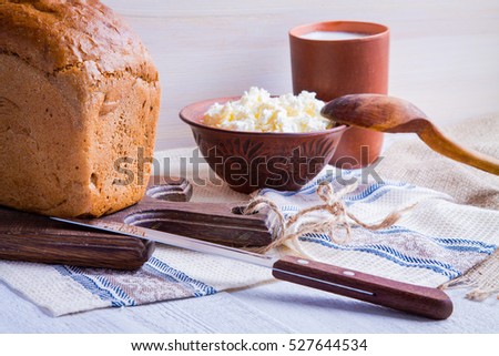 Cottage cheese in a clay plate, cup with milk and a loaf of bread on a white wooden background. Country style
