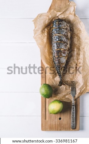 Baked fish with lime on parchment paper and cutting board on a white background of the old wooden boards vintage top view
