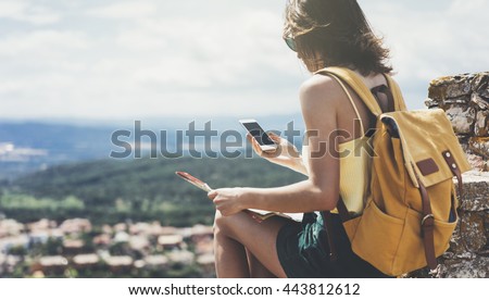 Hipster young girl with bright backpack looking at a map. View from back of the tourist traveler on background mountain, sea. Mock up for text message. Female hands using smartphone, holding gadget