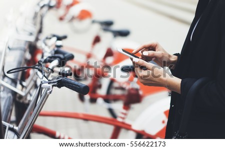 Young businesswomen in black  suit and umbrella using smartphone, biking and going to work by city bicycle on urban street, hipster girl holding mobile gadget, ecology environment concept