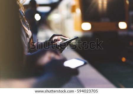 Enjoying travel. woman waiting on station platform on background light electric moving train using smart phone in night. Tourist texting message and plan route of stop railway, railroad transport
