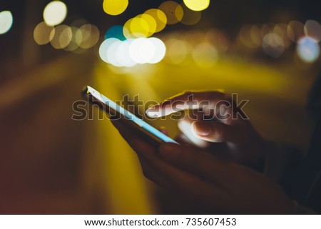 Girl pointing finger on screen smart phone on background illumination glow bokeh light in night atmospheric city, hipster using in hands mobile phone, mockup lights street, online internet concept