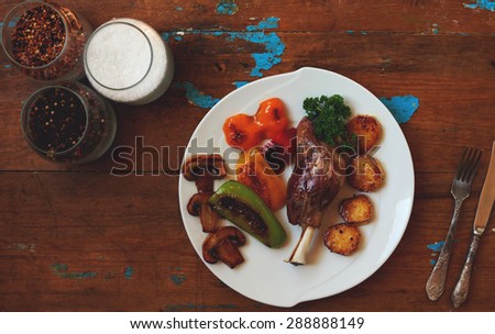 White plate with lamb shank lies on the old wooden table are located on the right side vintage silver cutlery, wife cooked dinner of roast lamb with vegetables and mushrooms