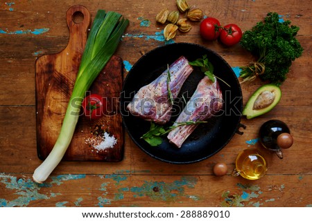 chef trendy steakhouse marinating lamb shank with rosemary and spices, onions parey and fresh tomatoes cooked  for spring salad, lamb marinated in a cast iron pot, lies next to the board for cutting