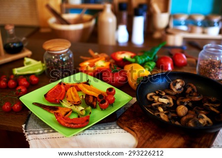 In the kitchen of the restaurant chef cooked peppers and tomatoes on the grill and put everything nicely on a bright plate, lay beside fresh tomatoes and pepper
