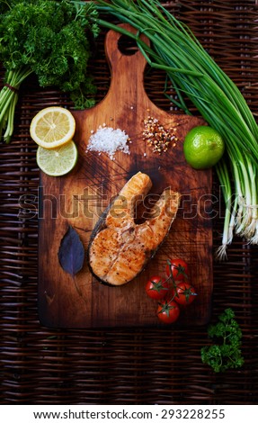 Big salmon steak baked in the oven until golden brown lying on a wooden surface, for serving fish perfect tomatoes chives and lemon, cook restaurant cooked piece of salmon on the grill