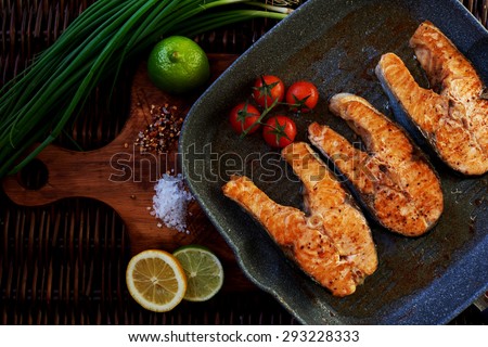 Fresh salmon steaks fried until golden brown, they are served in the rustic grill pan and serve with lemon tomatoes and onions