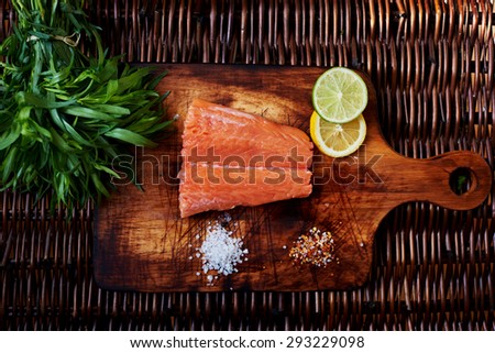 Chef ready to pickle fresh salmon steak. A small piece of salmon is on the board for cutting meat and fish is scattered next to the salt and pepper