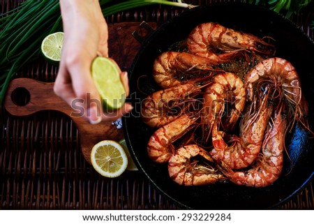Waitress fish restaurant prepares to issue customers with prawns, fresh seafood are served with lime and green onion, Tiger shrimps fried on a grill in a deep cast iron skillet