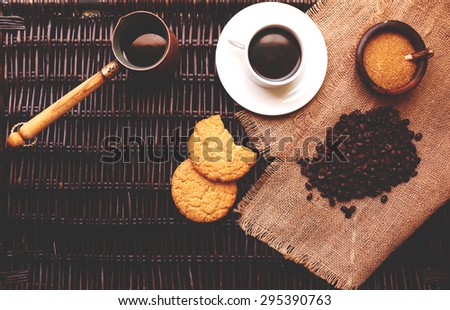On the table lies a dark rattan linen beige fabric on top of the tissue is a mug with hot coffee premium, two round macaroons lie close