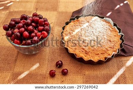 Housewife cooked tea cake with berries, close to the round shape is a deep glass dish with cherries