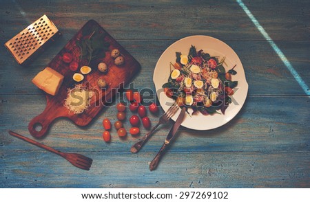 A simple recipe salad of fresh greens, quail eggs and cherry tomatoes, filling may be different, to serve the salad on a large white plate, side by side on a wooden board is grated parmesan cheese