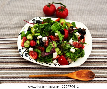 Bright fresh summer salad with cherry tomatoes, arugula, and a mix of various herbs, feta cheese is cut into small pieces, the salad served on big white plate