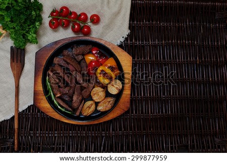 The meat cut into long thin slices, cook laid out in a round cast-iron skillet, along with meat baked peppers and onions until golden brown, cooked tomatoes and greens on salad