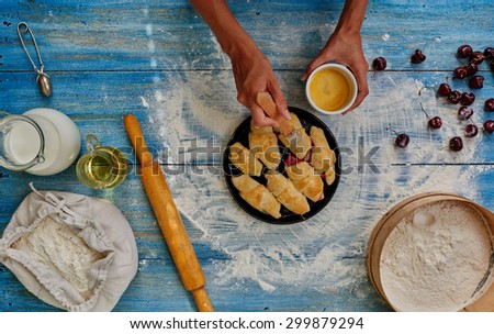 Female hands smeared with egg cakes before you put it in the oven to bake, which lies next to a rolling pin rolling out dough for roguelike