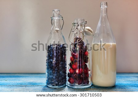 Three pitchers are on a wooden table in one poured milk in the other two falling asleep berries
