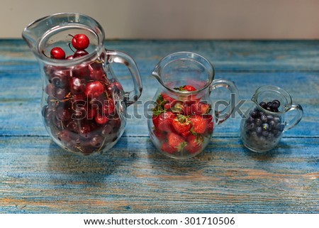 On the vintage wooden table, there are three glass carafe which are prepared fresh berries for cooking compote