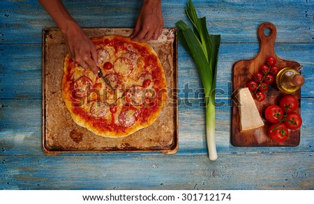 Housewife got pizza from the oven, cut it so that it has cooled down, side by side on a wooden board lying on the salad ingredients