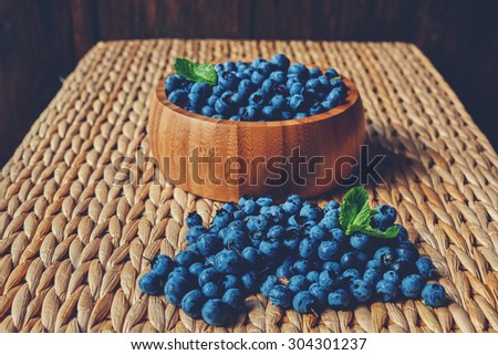 On the table is a light rattan deep wooden plate light wood, which sprinkling fresh ripe blueberries