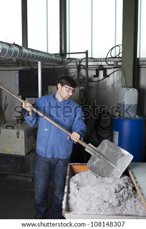 Worker cleaning waste with a shovel in factory