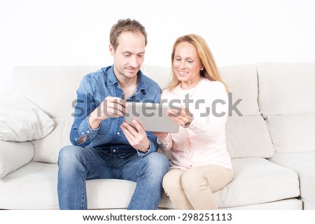 Elderly son looks with his mother at an device in living room