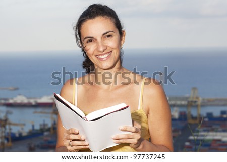 Latin woman reading a book outside with panorama behind
