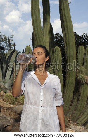 Woman drinking from water bottle in front of a cactus