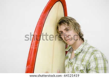 A male surfer looks thoughtfully out of frame whilst holding his surf board. Studio isolation with copy space surrounding the image.