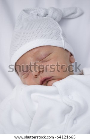 A close up shot of a new born baby less than one week old. He lays asleep on a white backdrop in white clothing. studio set up of one key light and a bounced flash with a shallow depth of field.
