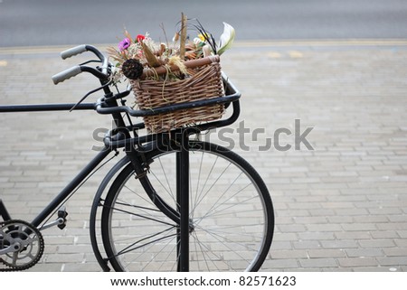 an old bike with a basket of flowers on the front shot under natural sunlight with a horizontal composition and space for text to the right.
